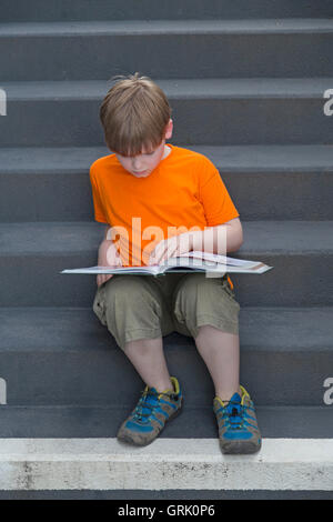 young boy reading a book sitting on stairs Stock Photo