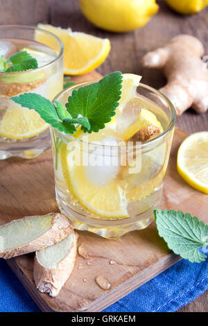Ginger ale soda with lemon, mint, ginger and ice over rustic wooden background