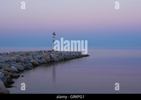 Lighthouse at Sunrise on the Rocky Coast. Dawning and Calm Sea in the Background. Stock Photo