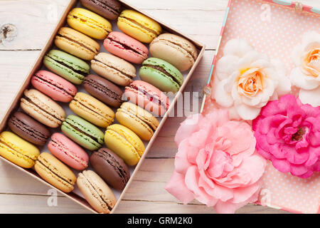 Colorful macaroons and rose flowers on wooden table. Sweet macarons in gift box. Top view Stock Photo
