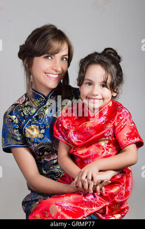Mother with little daughter dressed in beautiful chinese blue and red dresses posing happily embracing for camera, studio background Stock Photo
