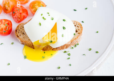 Poached egg on piece of wholegrain bread with vegetables and herbs close up Stock Photo