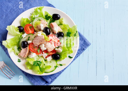 Tuna salad with tomatoes, black olives, rice, feta cheese and greens over blue wooden background with copy space Stock Photo