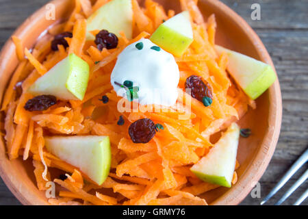 Carrot and apple salad with raisins, yogurt and herbs in rustic ceramic bowl close up Stock Photo
