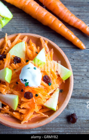 Carrot and apple salad with raisins, yogurt and herbs in rustic ceramic bowl close up Stock Photo