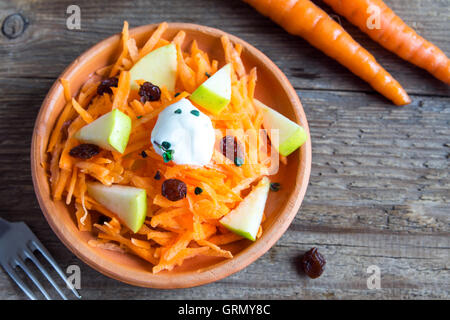 Carrot and apple salad with raisins, yogurt and herbs in rustic ceramic bowl, copy space Stock Photo