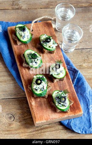 Mini sandwiches (snacks) with cucumber, olives and fish salad over rustic wooden background Stock Photo