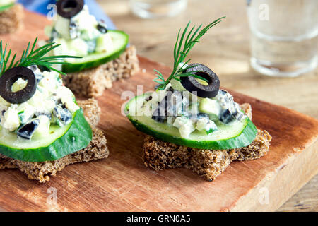Mini sandwiches (snacks) with cucumber, olives and fish salad over rustic wooden background Stock Photo
