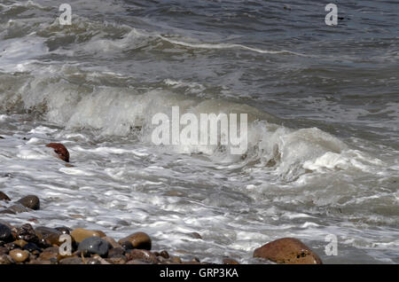 Waves breaking on a pebble-covered beach at Lindisfarne (Holy) Island in Northumberland, England. Stock Photo