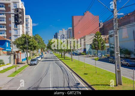 CURITIBA ,BRAZIL - MAY 12, 2016: long empty street with some autos parked at the sides and some trees on the sidewalk Stock Photo