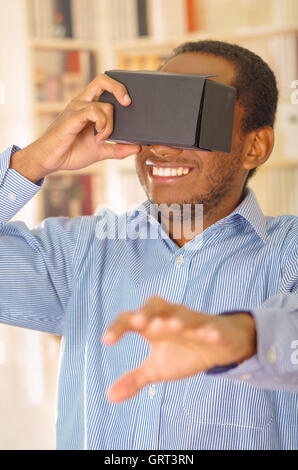 Man wearing blue shirt testing vitrual reality mobile device, holding glasses in front of eyes and smiling Stock Photo