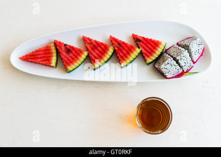 sliced watermelon and dragon fruit on plate with hot tea in the glass Stock Photo