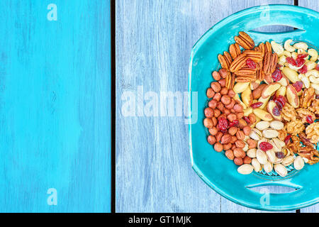 Nuts mix and cranberries on a plate, wooden surface background, top view with copy space. Stock Photo