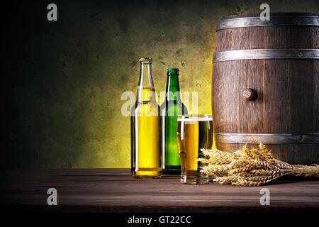 Full bottles of beer and glass with barrel against a dark background Stock Photo