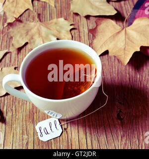 closeup of a white ceramic cup with a bag of tea or herbal tea being soaked in hot water, with the word fall written in its labe Stock Photo