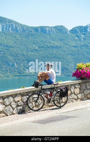 Male cyclist relaxing / resting while touring / riding in Conjux, on / beside Lake du Bourget (Lac Du Bourget) in Savoy, France. Stock Photo