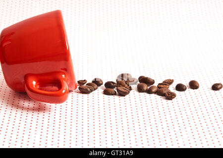 red cup for espresso coffee and coffee beans spilled out and scattered, coffee concept Stock Photo