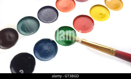 Paintbrush touching green watercolor paint cake on white background Stock Photo