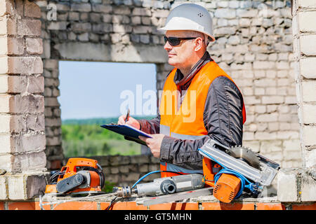 Construction worker writing near tools in unfinished building Stock Photo