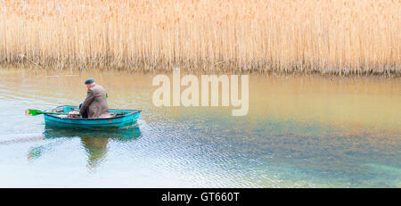 Man casting fishing line in lake with friend sitting in rowboat stock photo