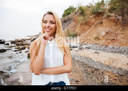 Smiling pensive young woman standing on the beach and thinking Stock Photo