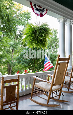 Comfortable wooden rocking chair on an outdoor patio with an ornamental white balustrade below the Stars and Stripes American fl Stock Photo