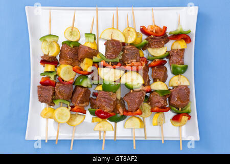 Tasty spicy marinated meat and vegetable kebabs displayed on a platter on their skewers ready for the summer barbecue, overhead Stock Photo