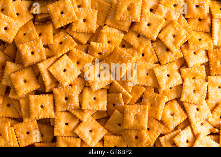 Background texture of square cheese crackers with central holes arranged in a layer viewed close up full frame from above Stock Photo