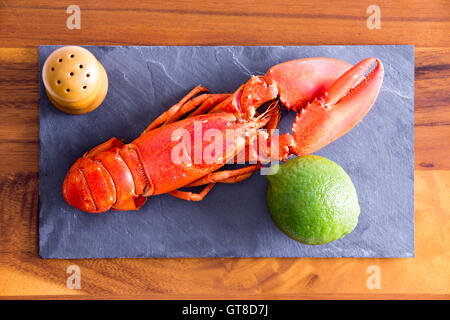 Close up High Angle Shot of Cooked Red Lobster on a Gray Cutting Board with Lime and Salt on Top of a Wooden Table. Stock Photo