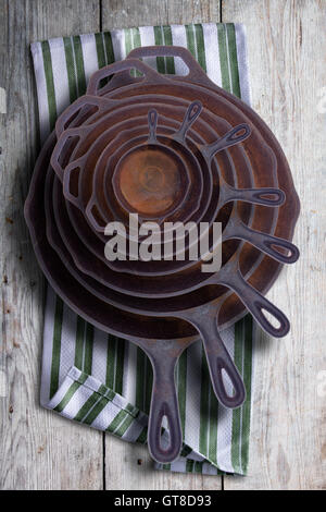 Collection of round rusty cast iron frying pans in diminishing sizes stacked one inside the other, viewed from above on a rustic Stock Photo