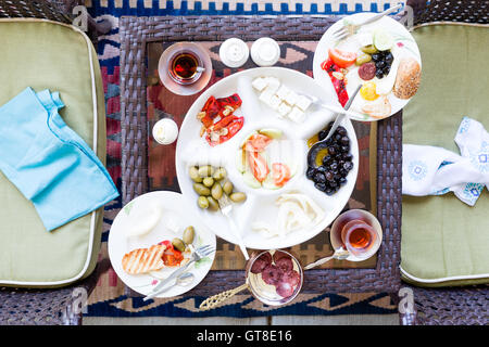 Unfinished Turkish breakfast on a patio table with a serving of fried eggs with a selection of fresh tomato, olives, cheese and Stock Photo