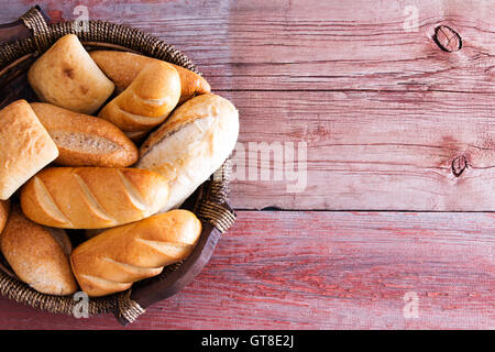 Bread basket filled with freshly baked golden crusty rolls in assorted shapes viewed overhead on rustic wooden boards with copys Stock Photo