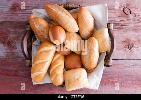 Assorted crusty fresh golden bread rolls in a basket in different speciality shapes displayed on a rustic wooden buffet table as Stock Photo