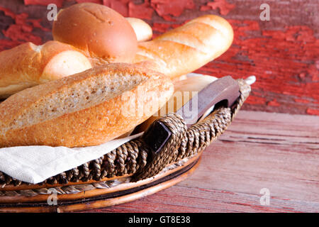 Basket of golden crusty fresh bread rolls in assorted shapes on a rustic wooden table ready to accompany dinner , close up side Stock Photo