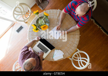 Discussion between two men seated at a round table decorated with yellow sunflowers using a laptop computer and paper documents, Stock Photo