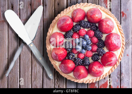 Fresh berries homemade tart with serving utensils, placed on a rustic wooden table. Above view. Stock Photo