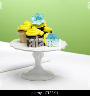 chocolate and vanilla cupcakes with yellow icing and blue sugar flowers on a cake stand Stock Photo