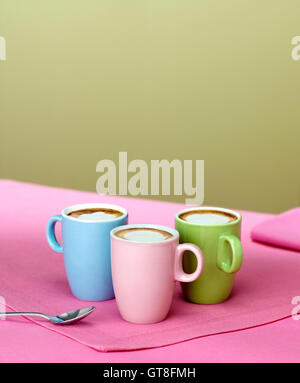 Trio of Pastel Coloured Demitasse Cups with Espresso and Foamed Milk on Pink Placemat with Spoon Stock Photo