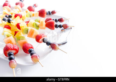 Serving of colorful healthy tropical fresh fruit kebabs with an assortment of exotic fruit on a white platter for a tasty vegan Stock Photo