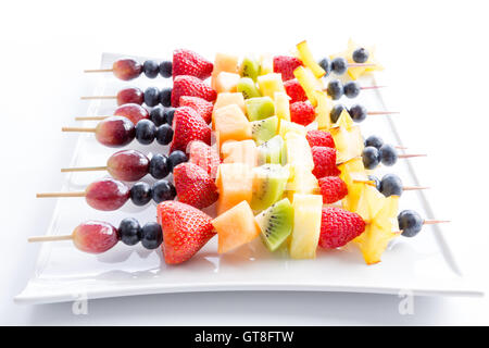 Serving of colorful fresh tropical fruit kebabs on a modern rectangular white plate viewed low angle with receding perspective o Stock Photo