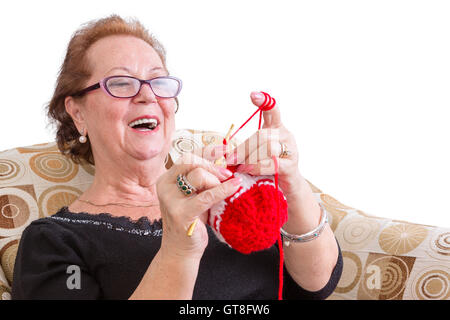 Happy elderly lady enjoying a joke laughing as she concentrates on her colorful festive red knitting while relaxing in a comfort Stock Photo