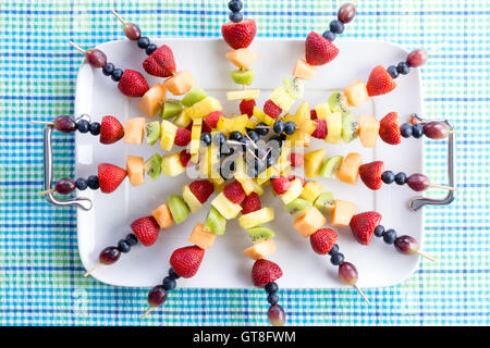 Presentation of colorful healthy fresh fruit kebabs on a summer picnic table made with seasonal exotic and tropical fruit for a Stock Photo