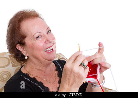 Laughing elegant senior lady sitting knitting a colorful red item as she enjoys her retirement, close up head and shoulders over Stock Photo