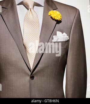 Detail of a light brown suit jacket with cream colored shirt and white handkerchief, yellow patterned necktie and yellow flower Stock Photo