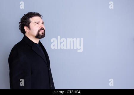 Three quarter view of hopeful attractive dark haired and bearded middle aged male in black shirt and blazer looking away over gr Stock Photo