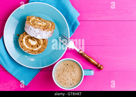 Top down view of two slices of roulo cake dessert and mug of coffee next to fork on napkin over light purple wooden table Stock Photo