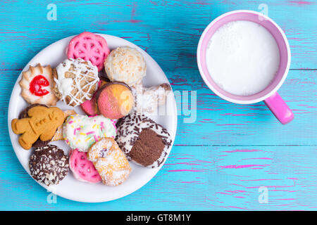 White plate full of sugary chocolate, strawberry, gingerbread and other flavored cookies next to pink cup of milk over crackled Stock Photo