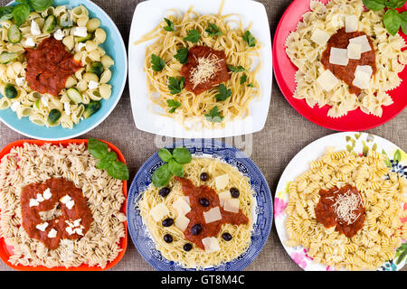 Top down view on six square and circular plates filled with different vegetables and pasta topped with herbs, sauce, cheese and Stock Photo