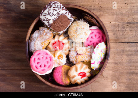 Bowl of colorful delicious assorted cookies with chocolate, glazed biscuits and decorative pink cookies in a rustic bowl on an o Stock Photo