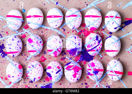 Colorful kids Easter eggs splattered in magenta pink and blue paint arranged in three neat rows over a beige background to celeb Stock Photo